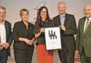 Jürgen Kroos, Präsident der HWK Münster, Ministerin Mona Neubaur (v. l.) und WHKT-Präsident Berthold Schröder (r.) nehmen die diesjährigen Ehrenamts-Preisträger, Nadine und Bernd Winkels, in ihre Mitte.